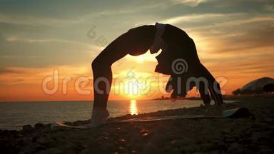 剪影年轻女子在海上日落时练习瑜伽。 快乐的生活时刻-海滩上的剪影瑜伽